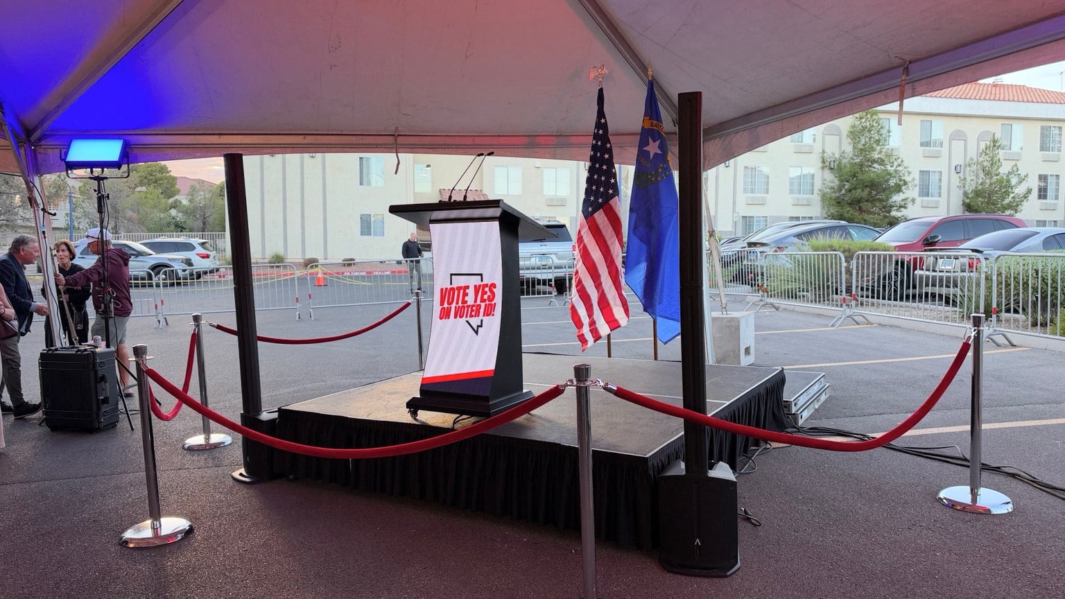 Microphone-equipped lectern on a small stage beneath a tent, with column speakers, U.S. and Nevada flags, and blue and red lighting
