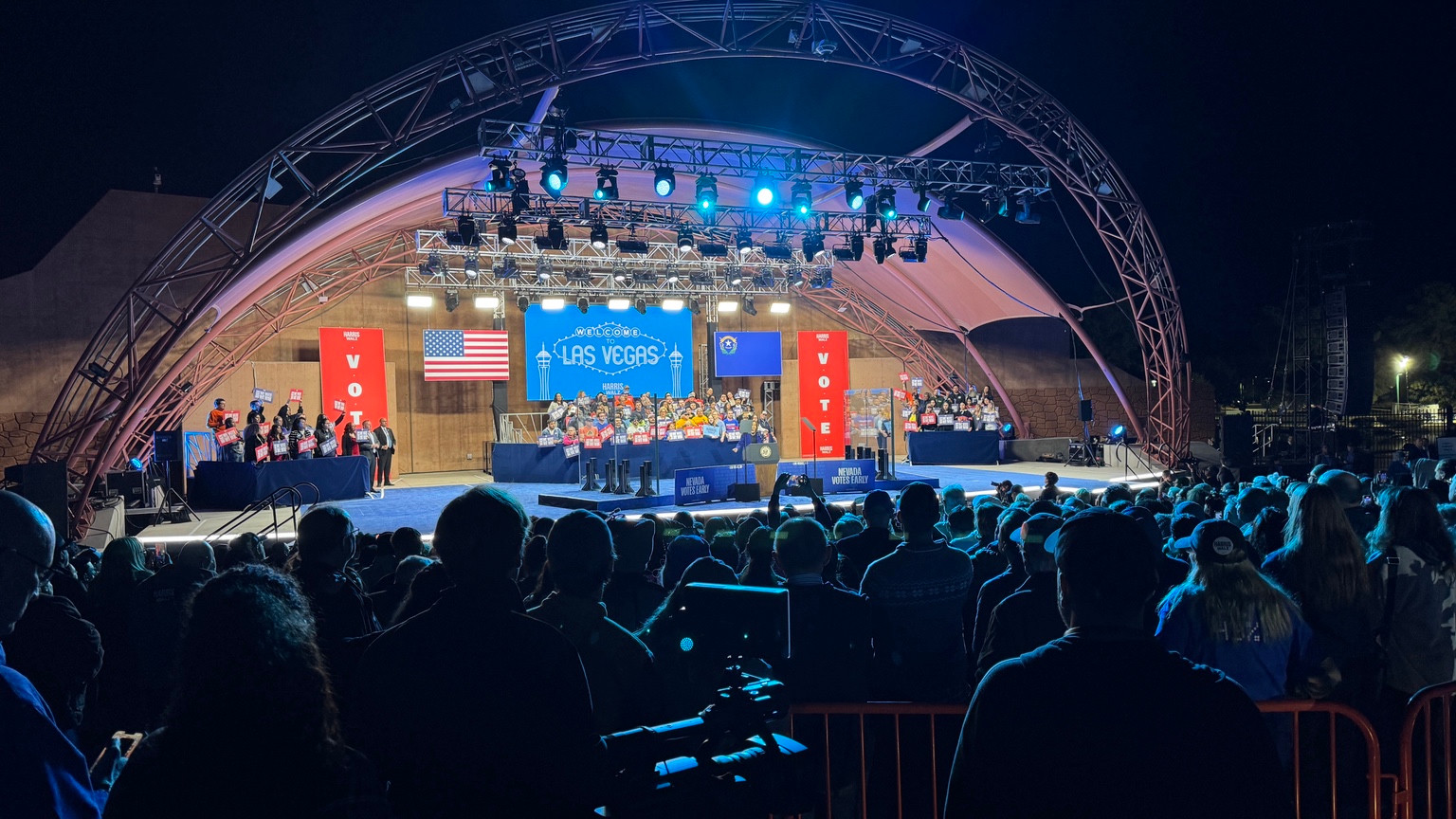 A Las Vegas Harris/Walz campaign event with an outdoor stage, lighting rig, screens, and audience